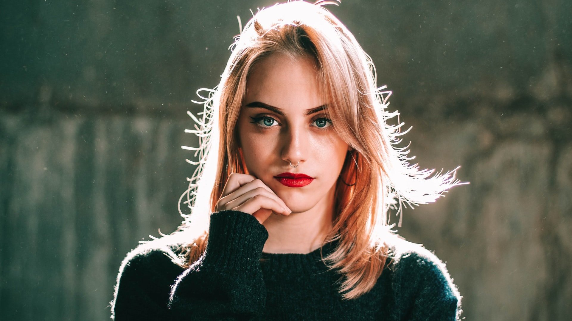 ErnAn Solozábal / Unsplash Mulher branca de cabelos loiros e batom vermelho com a mão na lateral do rosto.