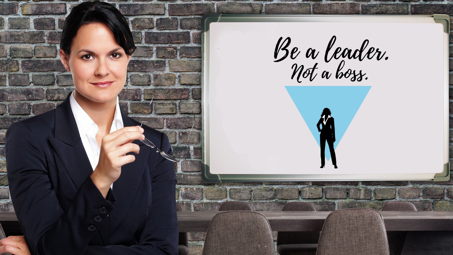 Uma mulher de negócios, trajada com um terno e segurando um óculos. Ao fundo, uma lousa com os dizeres be a leader, not a boss.