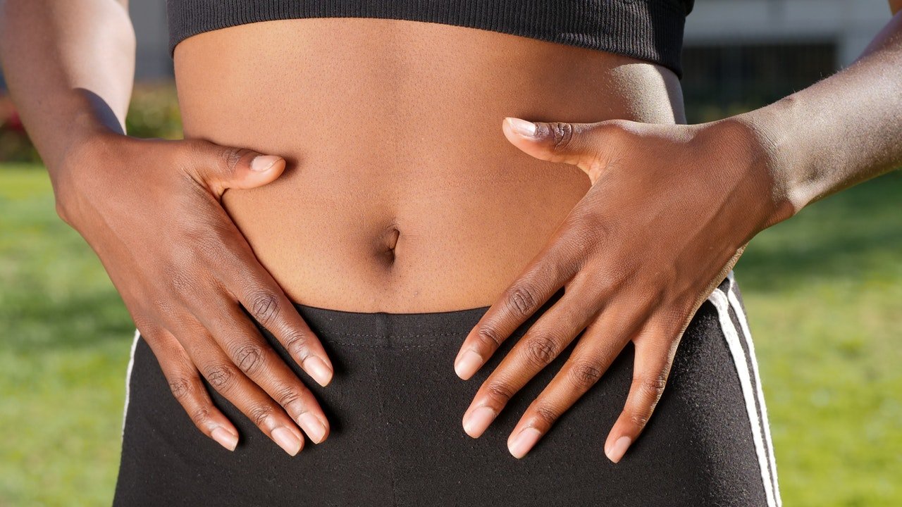 Uma mulher negra magra com as mãos apoiadas sobre a barriga