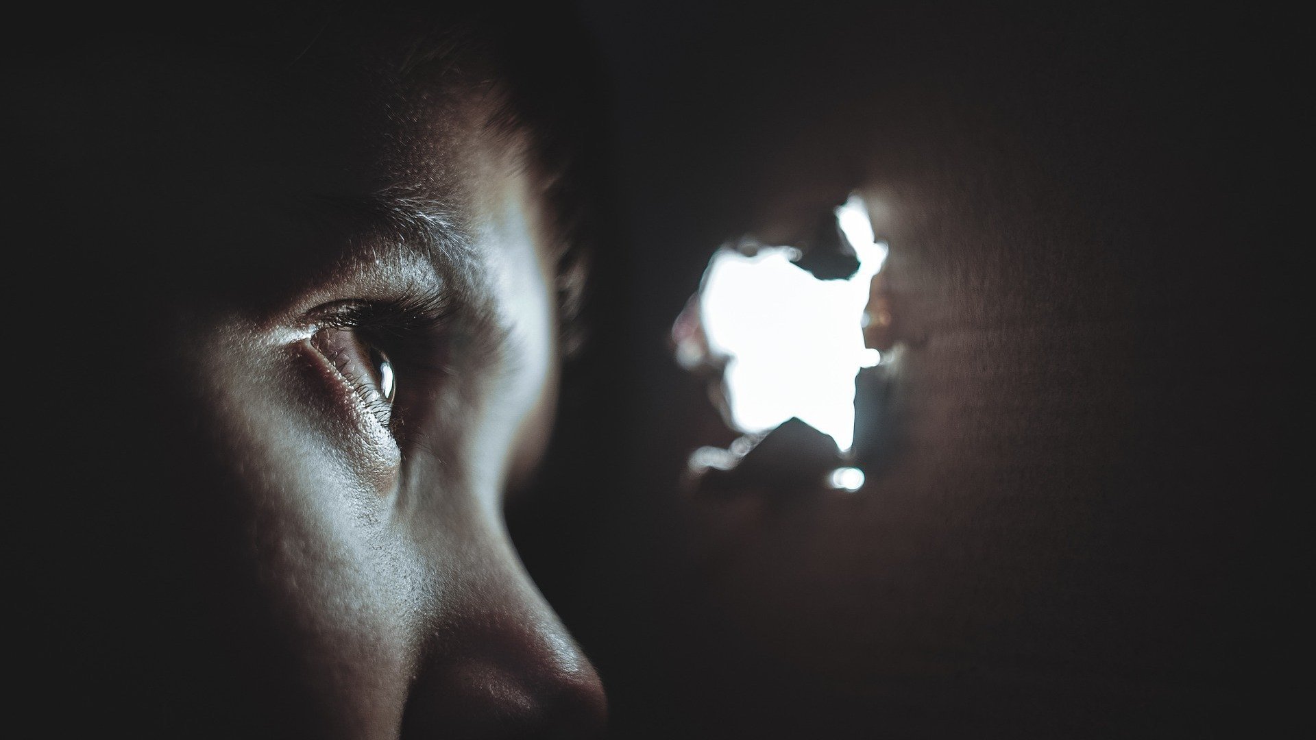 O rosto de um garoto, no escuro, observando uma fresta de luz