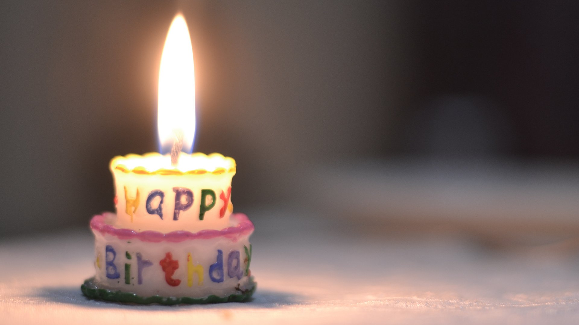Um minúsculo bolo de aniversário com uma pequena vela em cima dele. Há uma chama em cima da vela.