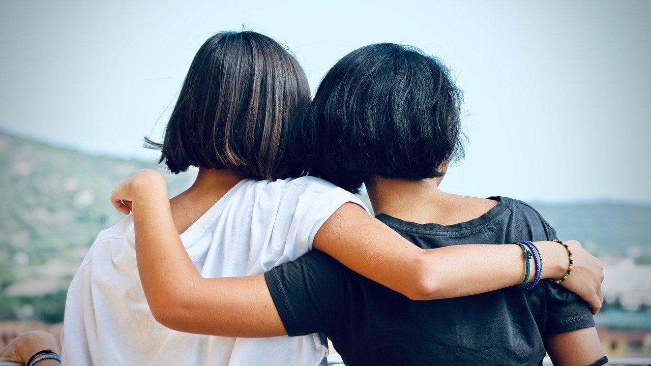 Vistas de costas, duas mulheres se abraçando.