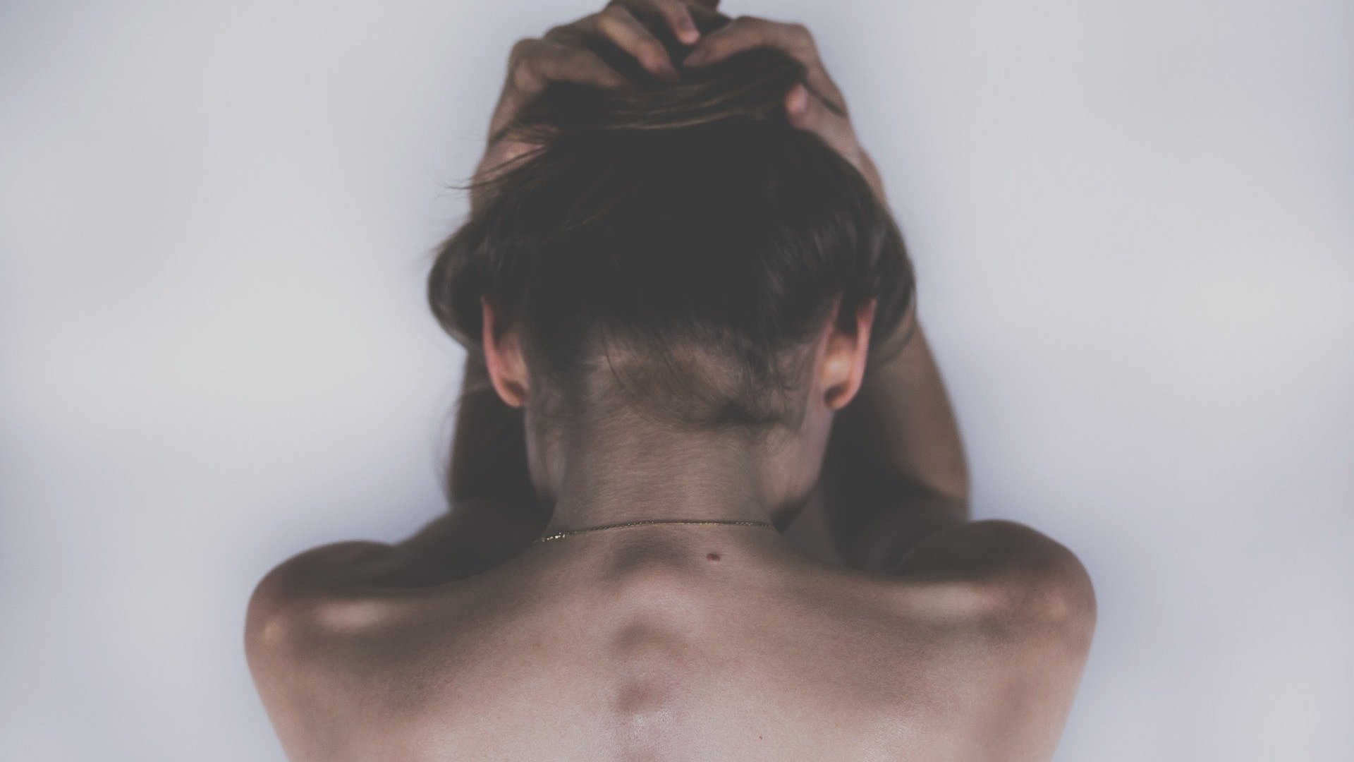 As costas e nucas de uma mulher vistas de um ângulo superior. Ela está com as mãos sobre a cabeça.