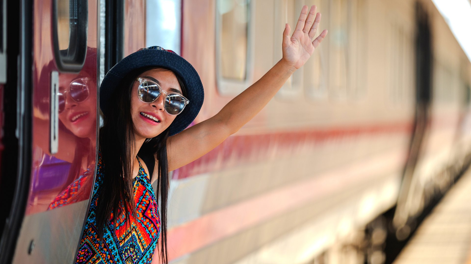 Uma mulher de chapéu e vestido acenando com parte do corpo esgueirando para fora de um trem.