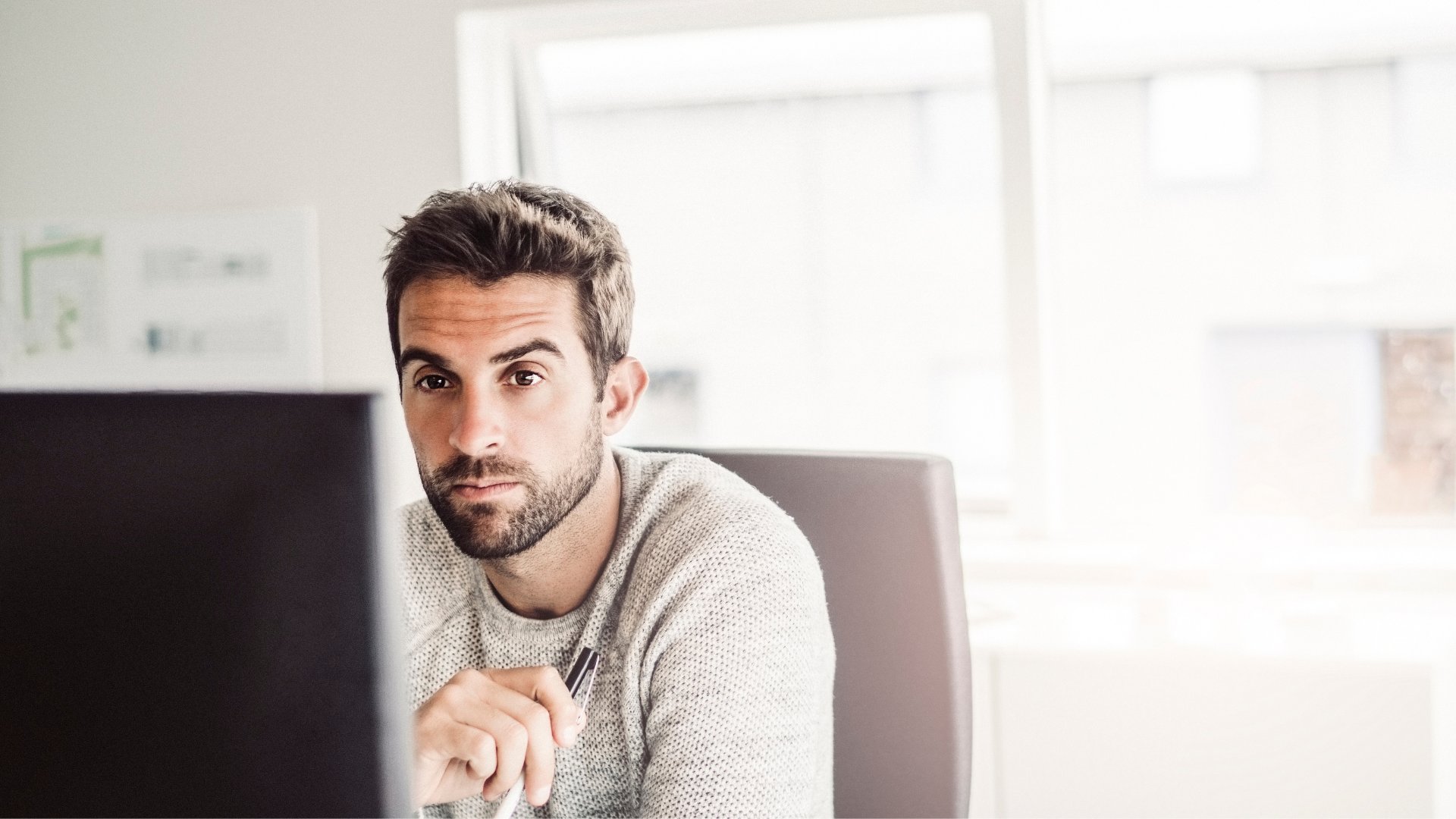 Um homem branco sentado olhando fixamente para um monitor.