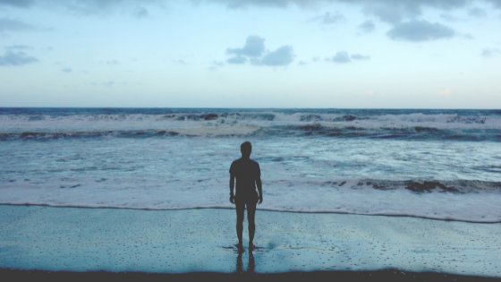Homem em pé na beira do mar ao amanhecer