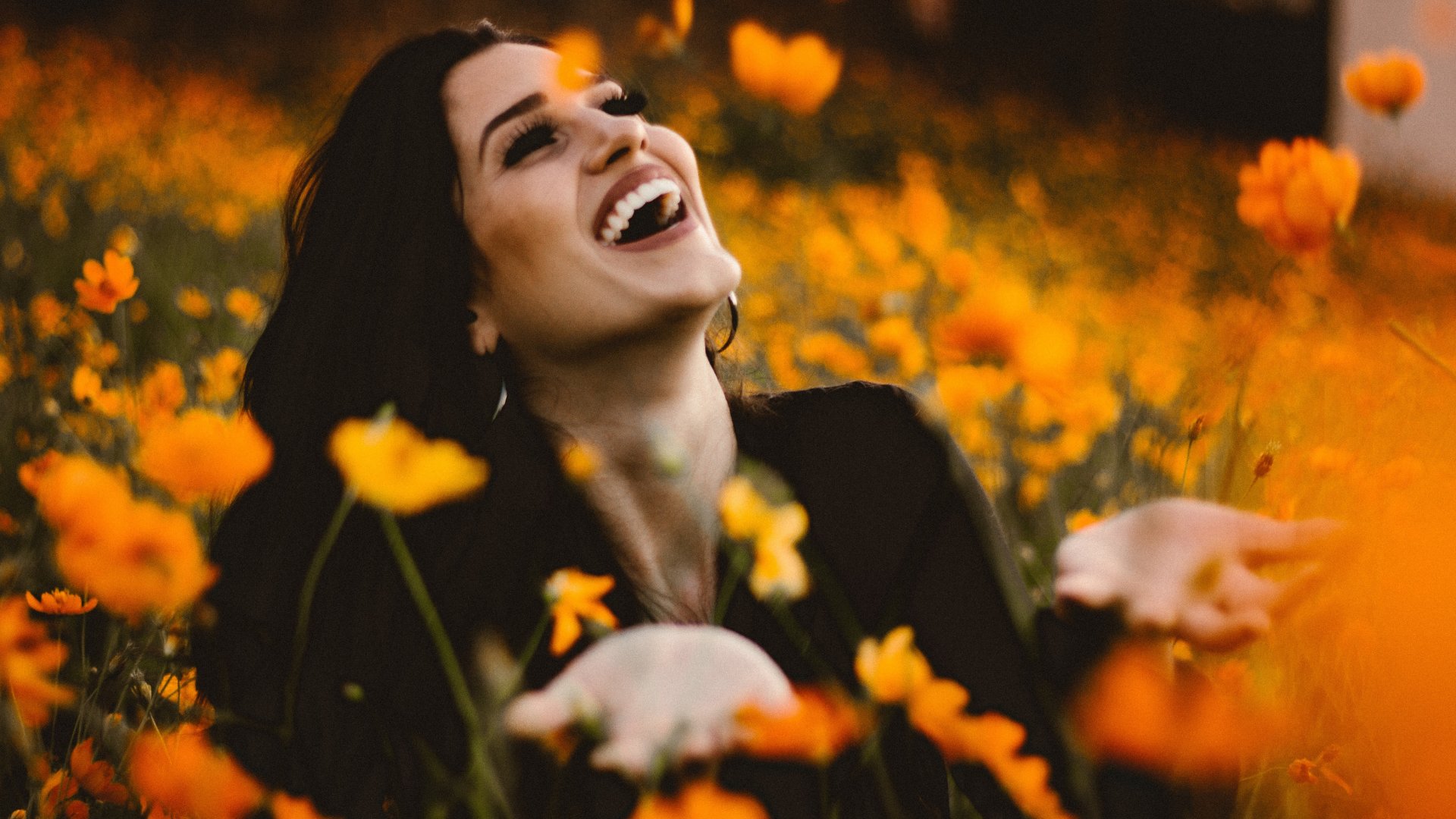 Uma mulher com a cabeça erguida pro alto. Ela está sorrindo sobre um campo florido.