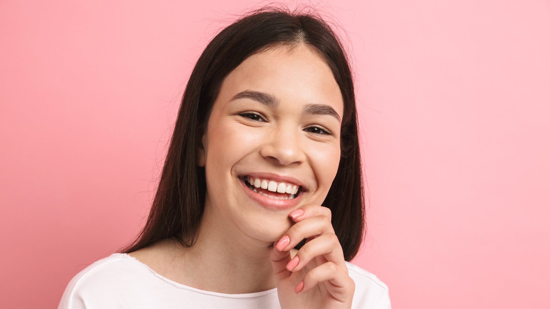 Uma mulher de cabelos pretos sorrindo. Ela coloca sua mão esquerda sobre seu queixo.