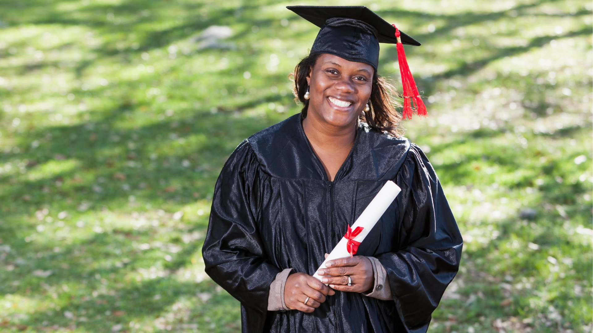 Uma mulher negra trajando uma beca e segurando um diploma.