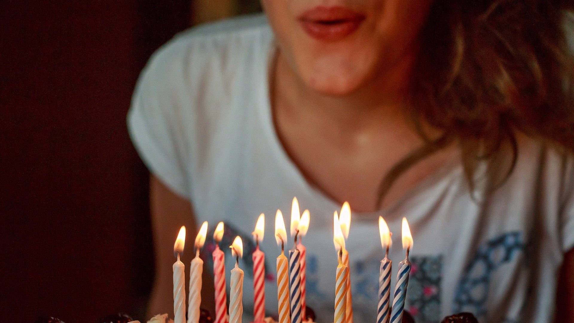 Uma mulher branca assoprando velas de aniversário.