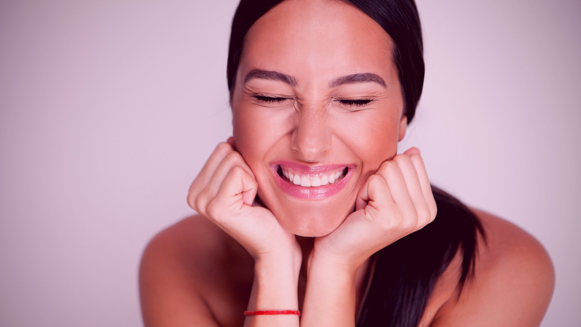 Uma mulher com as mãos sob o queixo sorrindo.