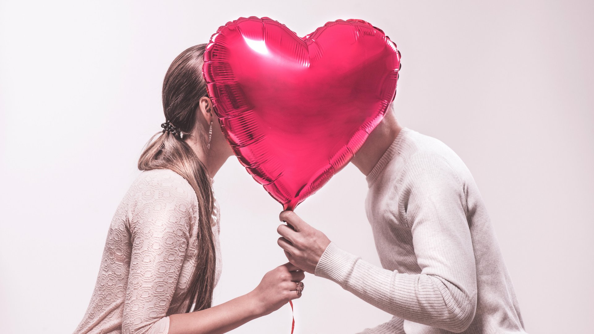 Uma mulher e um homem se escondendo atrás de um balão em formato de coração.