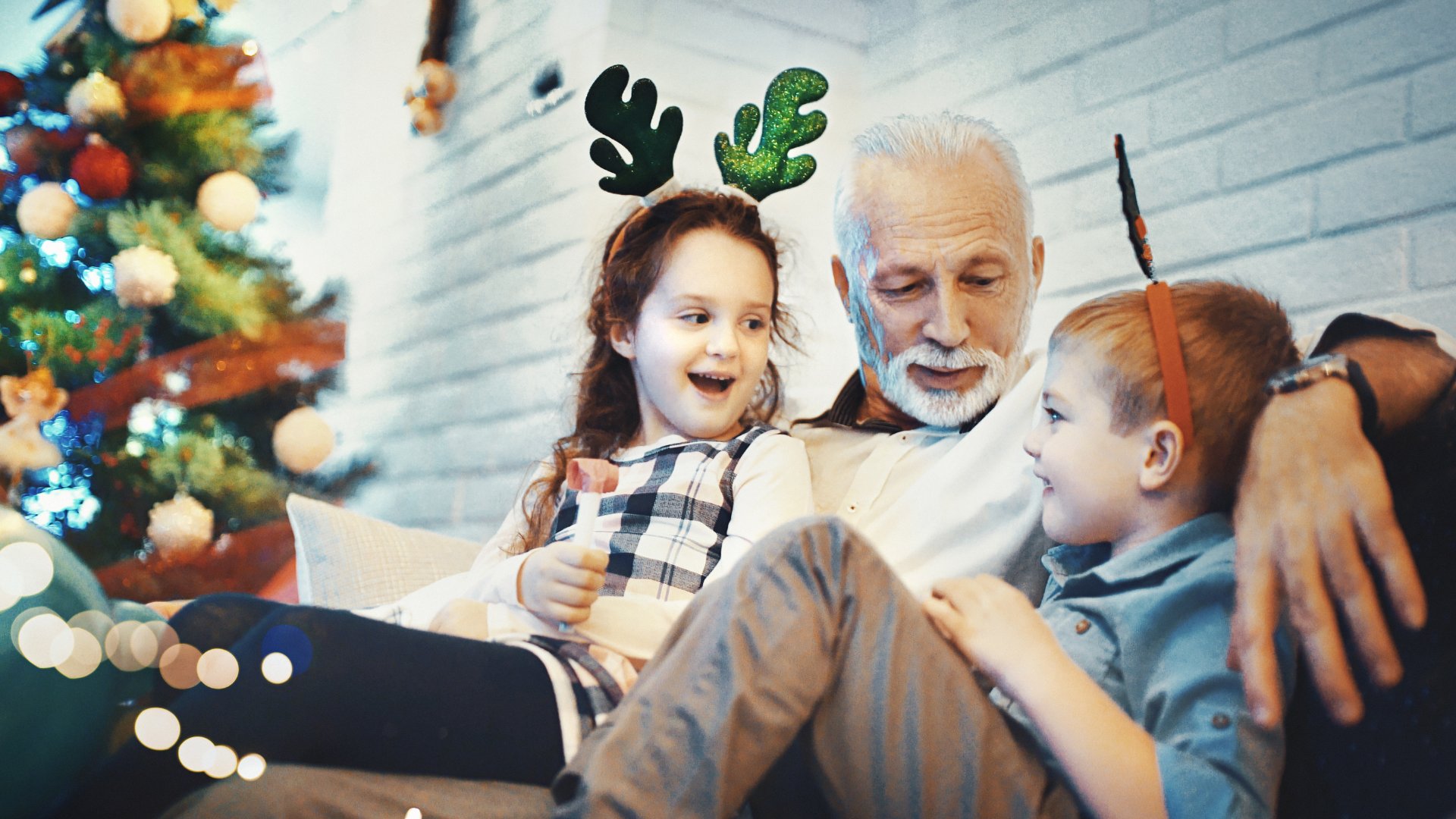 Um homem sentado próximo a duas crianças. À esquerda, uma árvore natalina.
