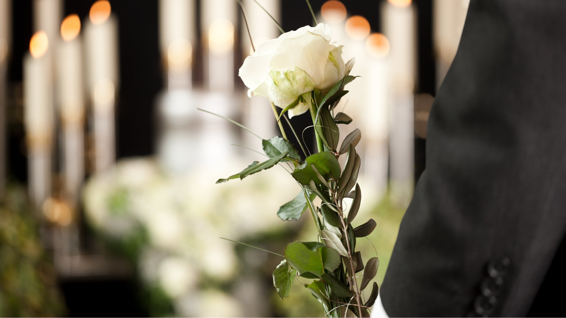Em primeiro plano, um resquício de um terno e uma flor branca. Ao fundo, velas desfocadas.
