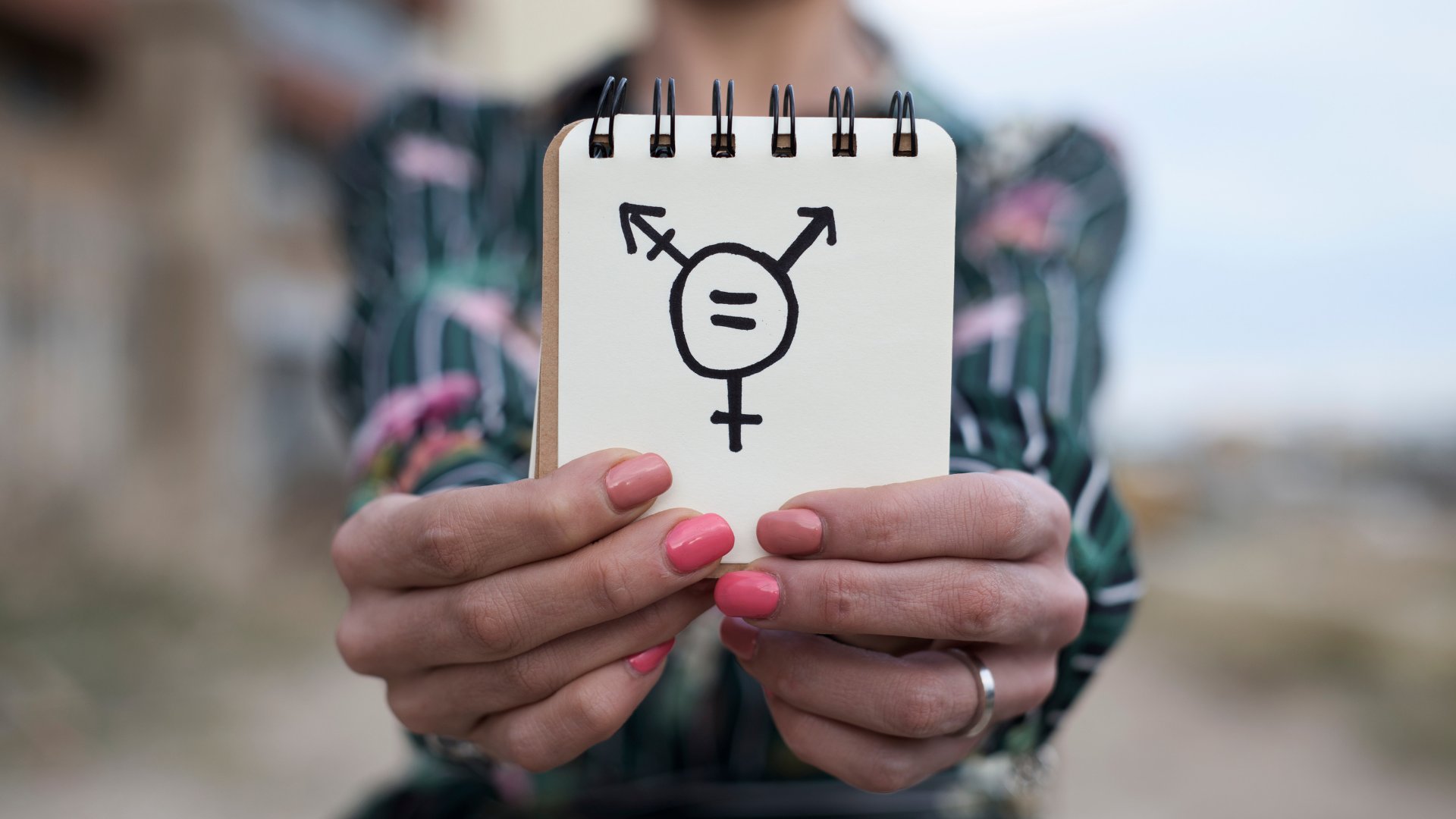 Uma pessoa segurando um bloco de notas que contém um desenho do símbolo transexual.