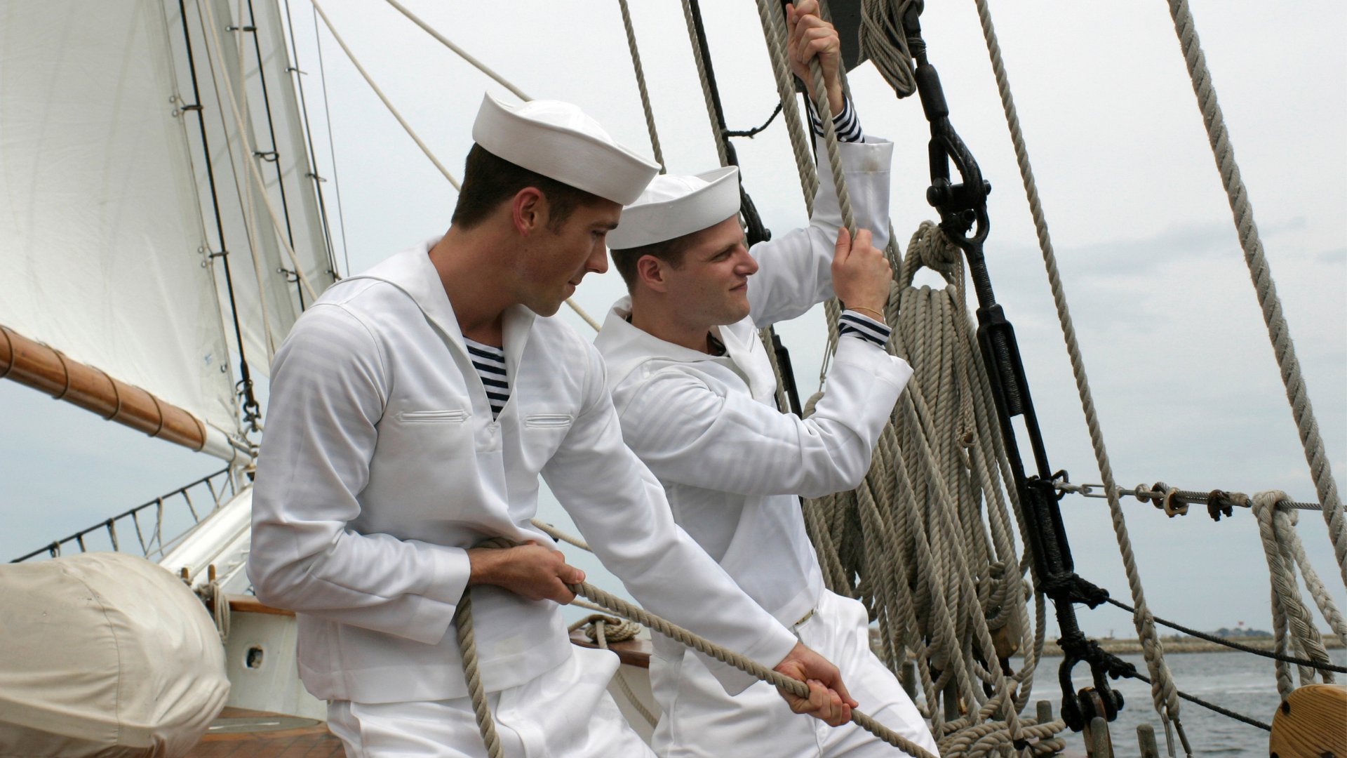 Dois marinheiros puxando cordas instaladas num barco.