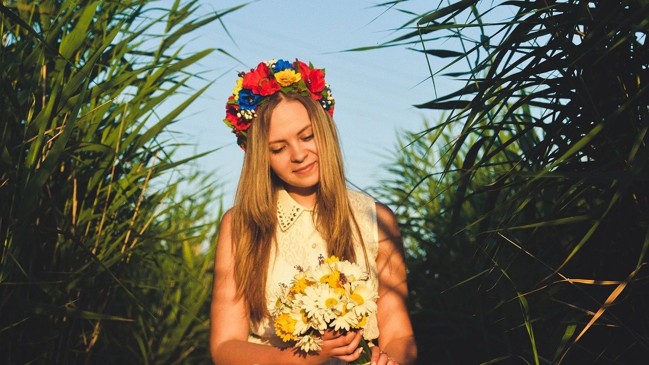 Mulher branca vestindo uma coroa de flores e segurando um buquê de flores no meio do mato