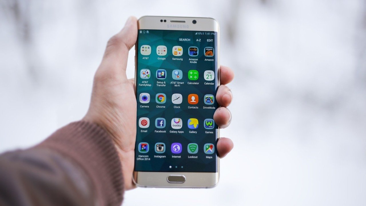 Mão branca segurando smartphone com menu de aplicativos aberto