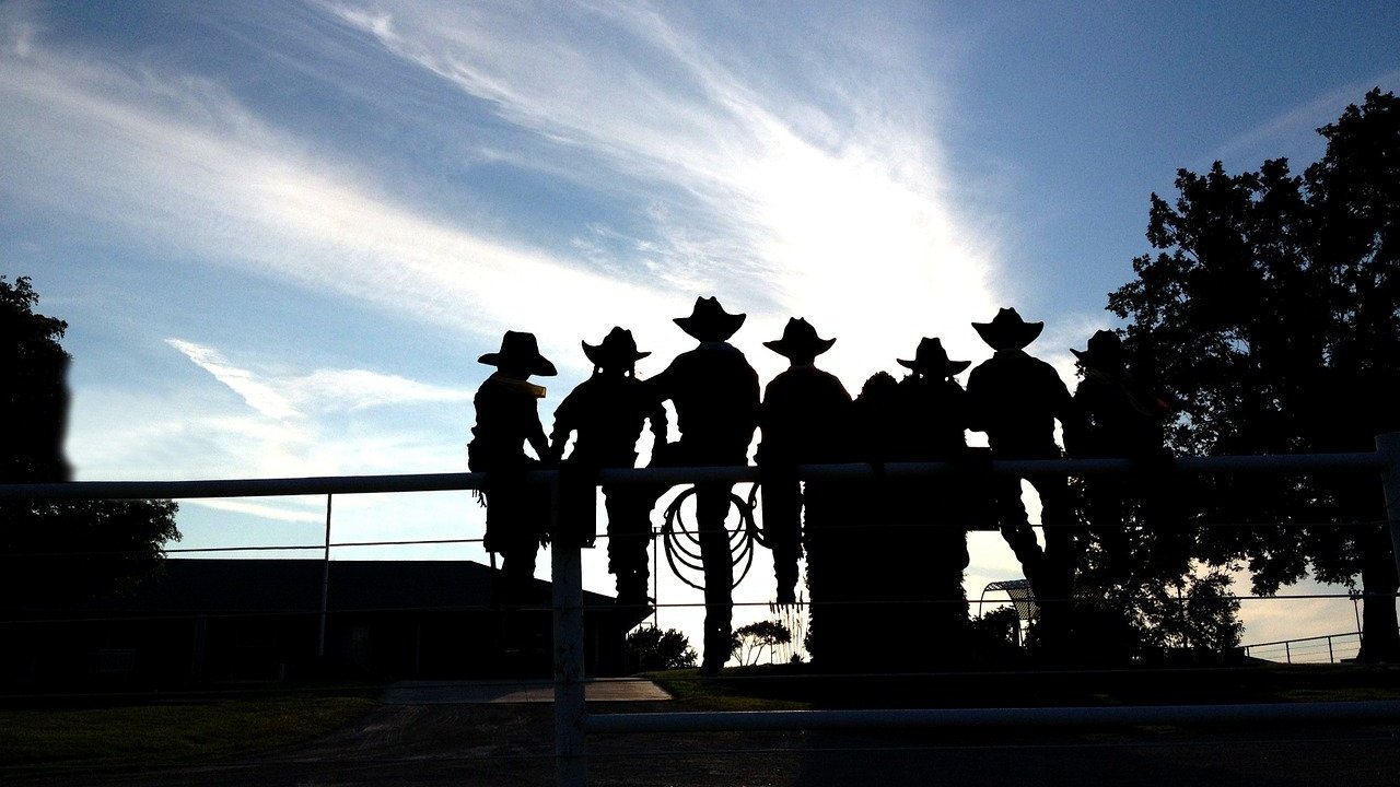 várias pessoas com chápeu de cowboy sentados numa cerca e de costas