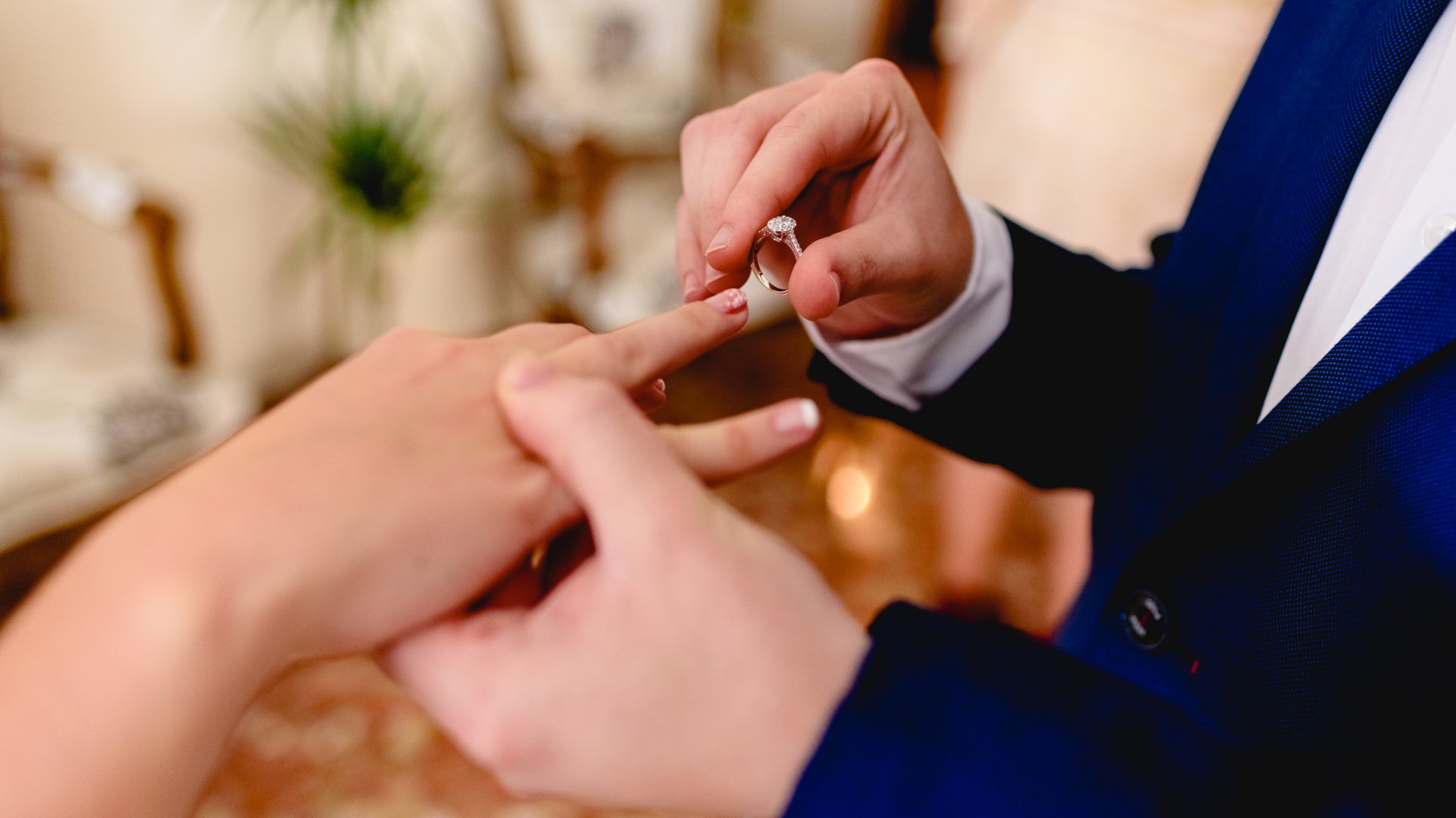 Uma aliança sendo colocada por uma mão masculina no dedo anelar de uma noiva.