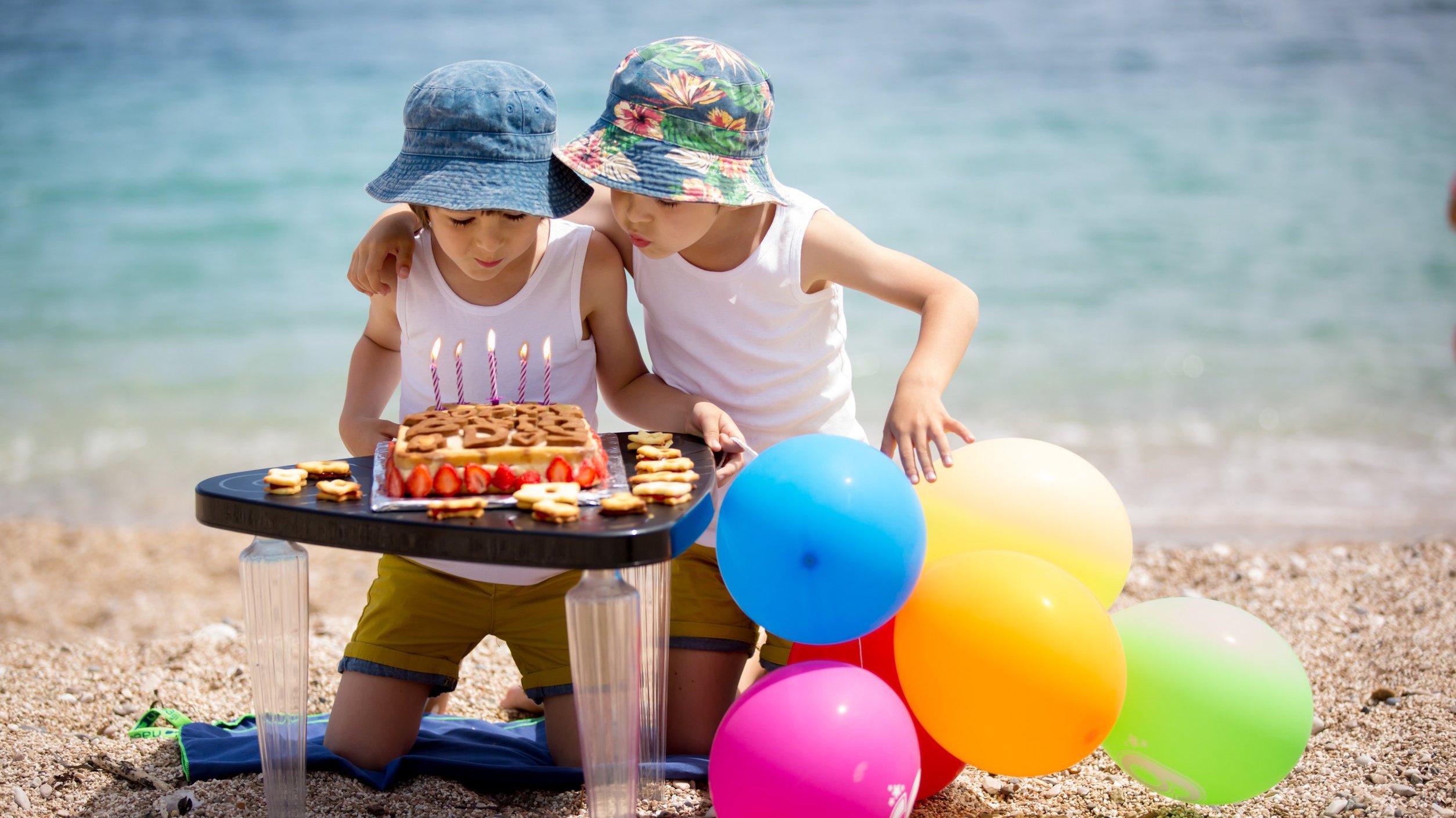 Duas crianças na praia assoprando as velas de um bolo de aniversário