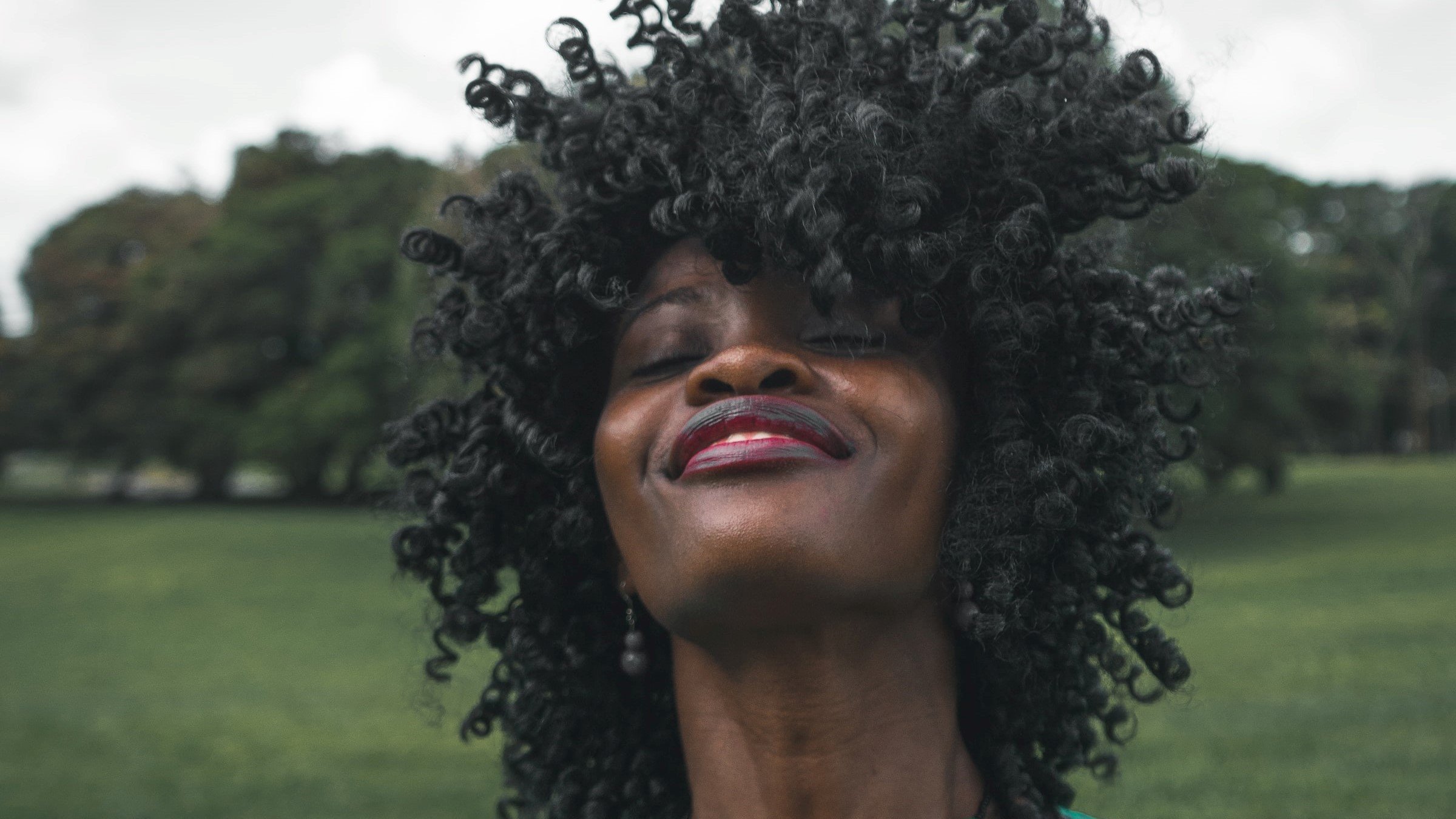 mulher com cabelo black power de olhos fechados e sorrindo