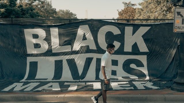 homem negro de máscara em frente a um grande cartaz que diz que vidas negras importam