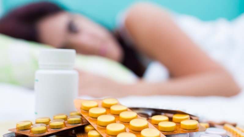 Mulher fora de foco na cama com  pílulas em uma mesa em primeiro plano