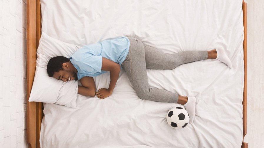 Homem dormindo com uma bola de futebol nos pés