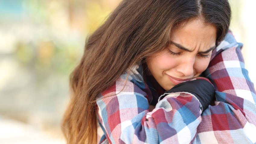 Menina chorando sozinha com os braços cruzados, encolhida