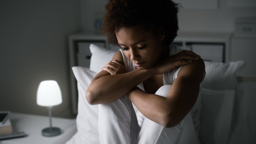 Mulher toda de branco sentada em uma cama