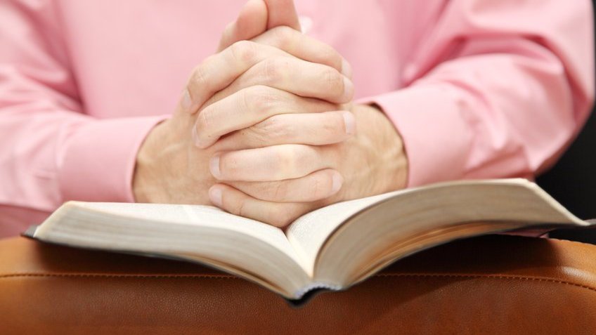 Mãos cruzadas com uma bíblia