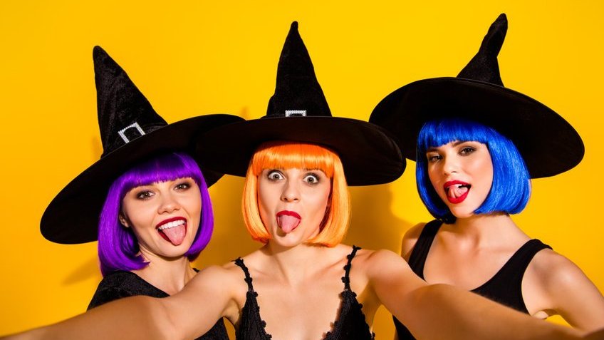 Três mulheres vestidas de fantasia de bruxa fazendo caretas tirando uma foto