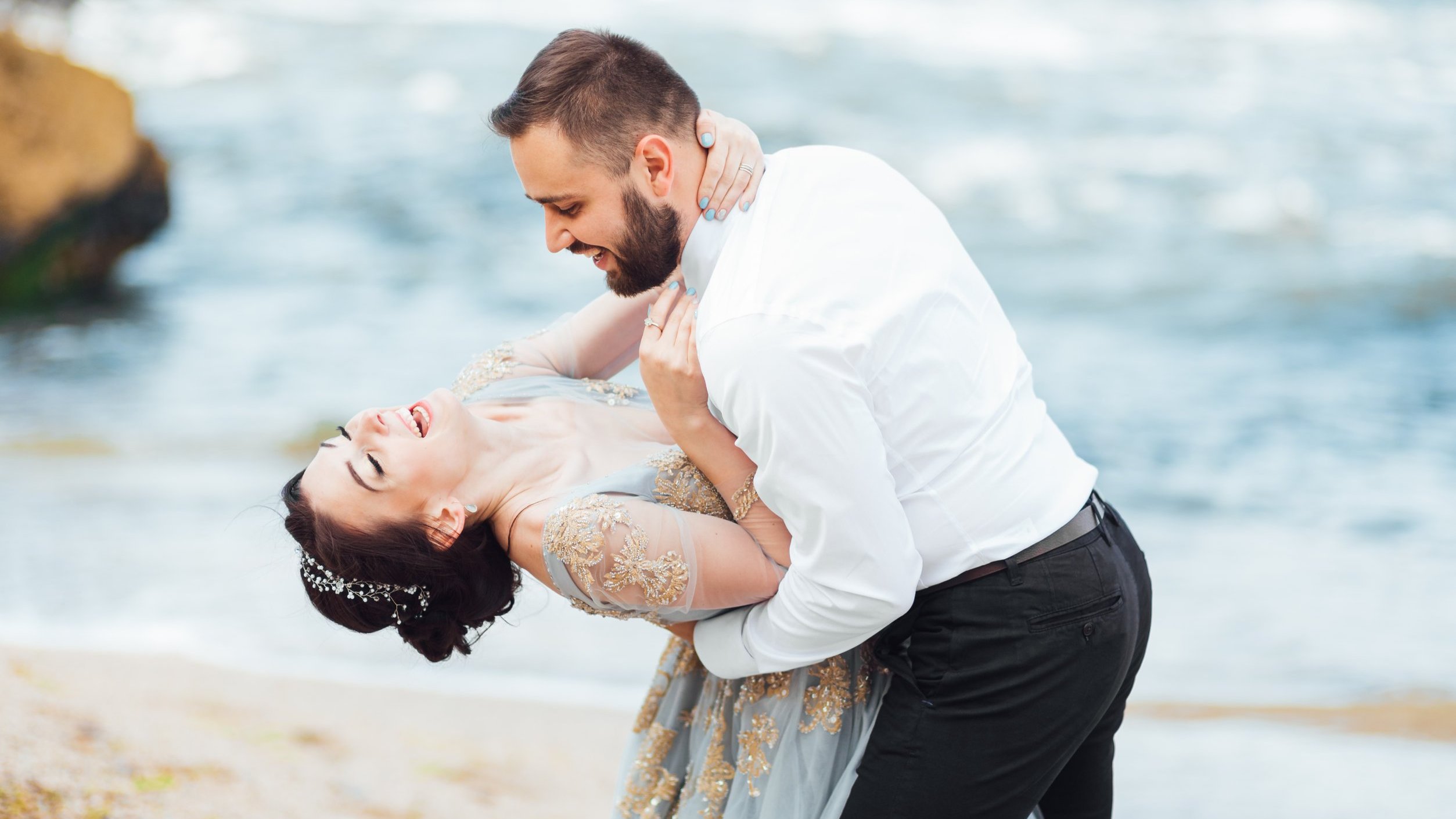 Casal rindo abraçado na areia da praia