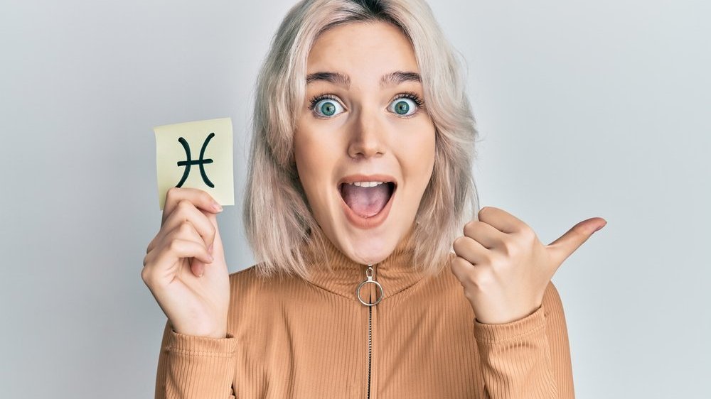 Mulher sorrindo fazendo positivo com uma mão e com a outra segurando um post-it com o símbolo de peixes desenhado