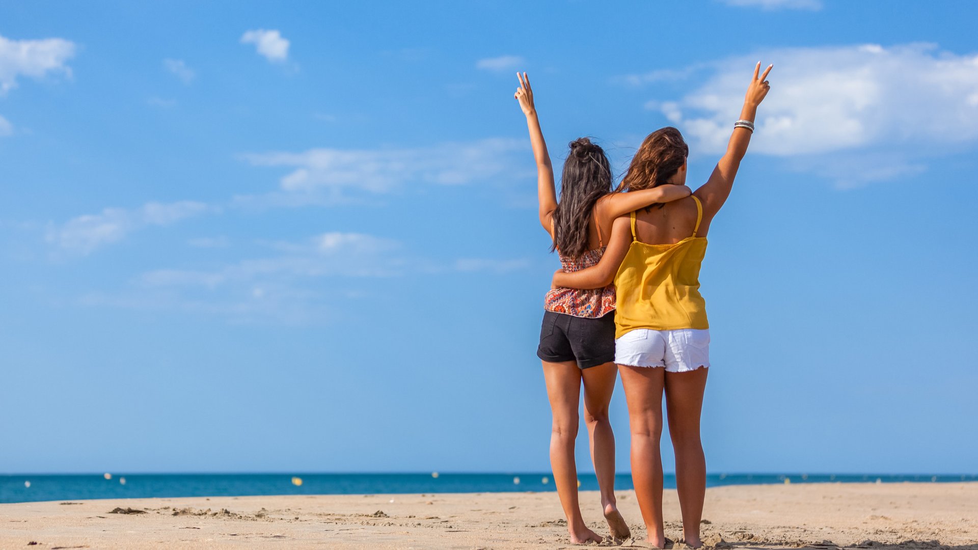 Mulher e menina de costas abraçadas em pé na areia da praia