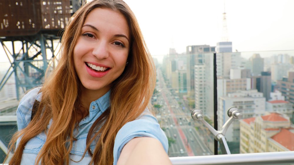 Mulher fazendo uma selfie com prédios ao fundo