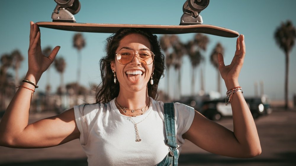 Mulher sorrindo e segurando um skate na cabeça