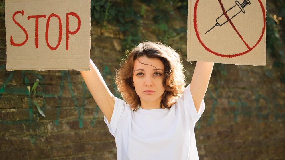 Mulher segurando cartazes contra vacinação