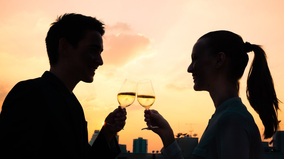 Um homem (à esquerda) e uma mulher (à direita) brindando taças de champanhe. Ambos estão sorrindo.