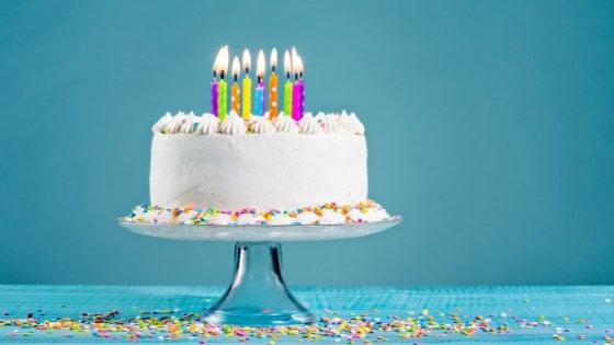 Bolo de aniversário branco com velas coloridas sobre fundo azul