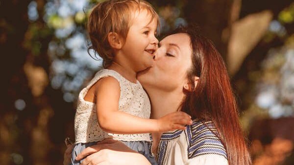 Mulher beijando a bochecha de uma criança pequena e sorridente.
