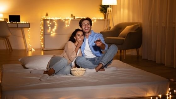 Prostock-studio / Shutterstock Homem e mulher assistindo, sorrindo e comendo pipoca.