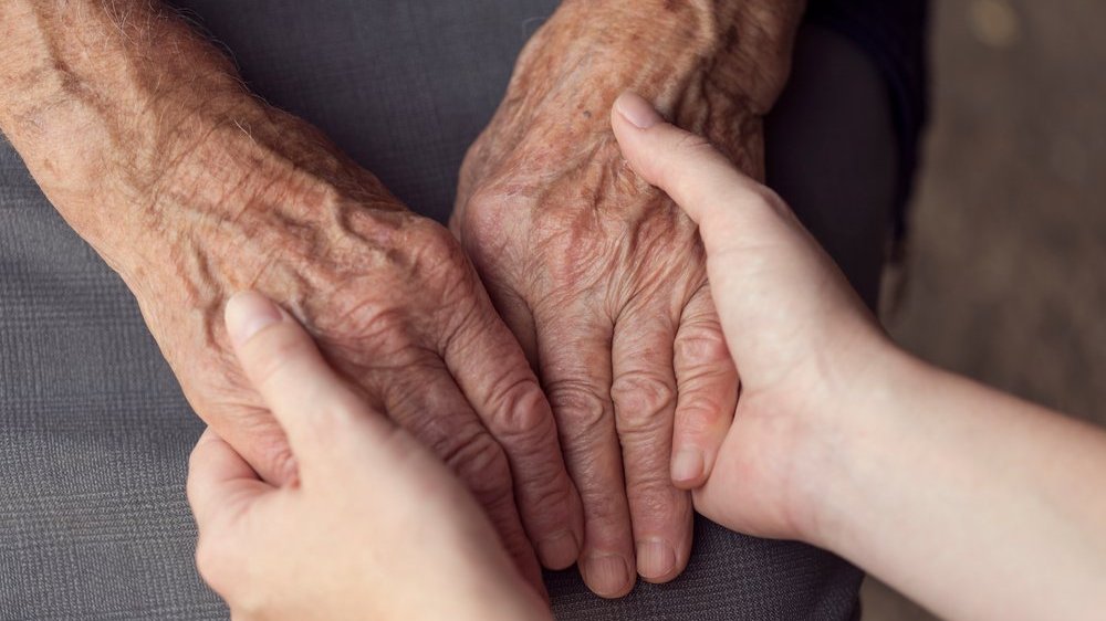 Mãos de pessoa idosa dando mãos para pessoa jovem