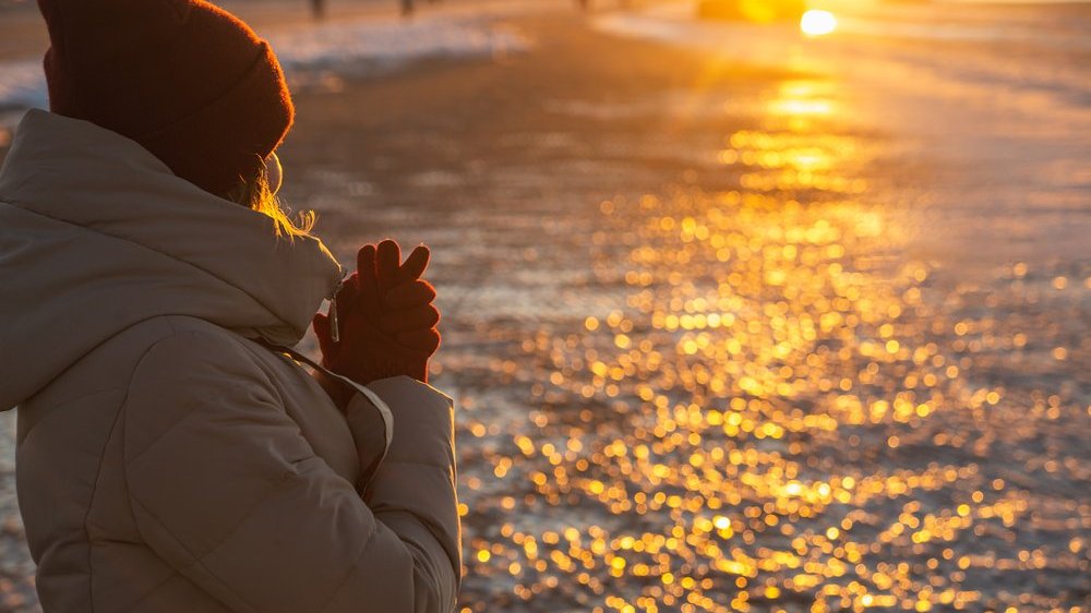 Mulher de costas vestindo roupas de frio olhando para a luz do sol