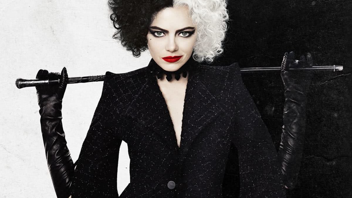 A atriz Emma Stone interpretando a personagem Cruella de Vil. Ela tem cabelos pretos e brancos e segura, atrás das costas, uma bengala.