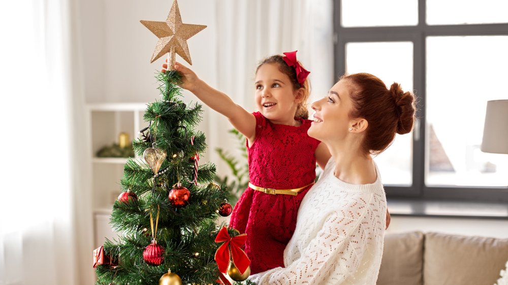 Syda Productions / Shutterstock Menina no colo da mãe, as duas montando árvore de natal