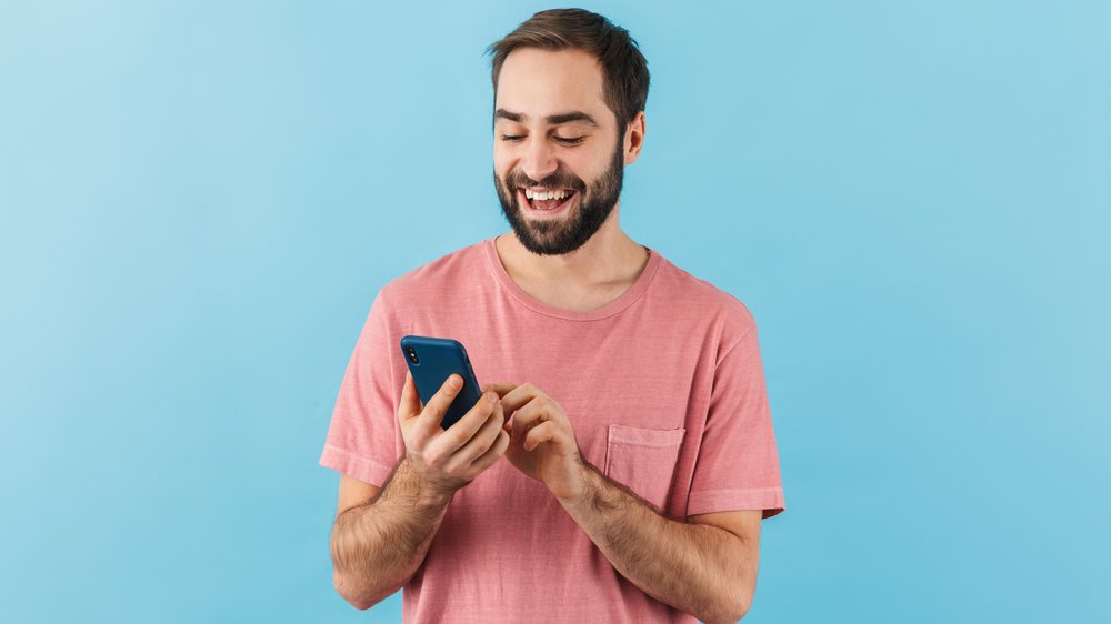 Homem mexendo no celular e sorrindo