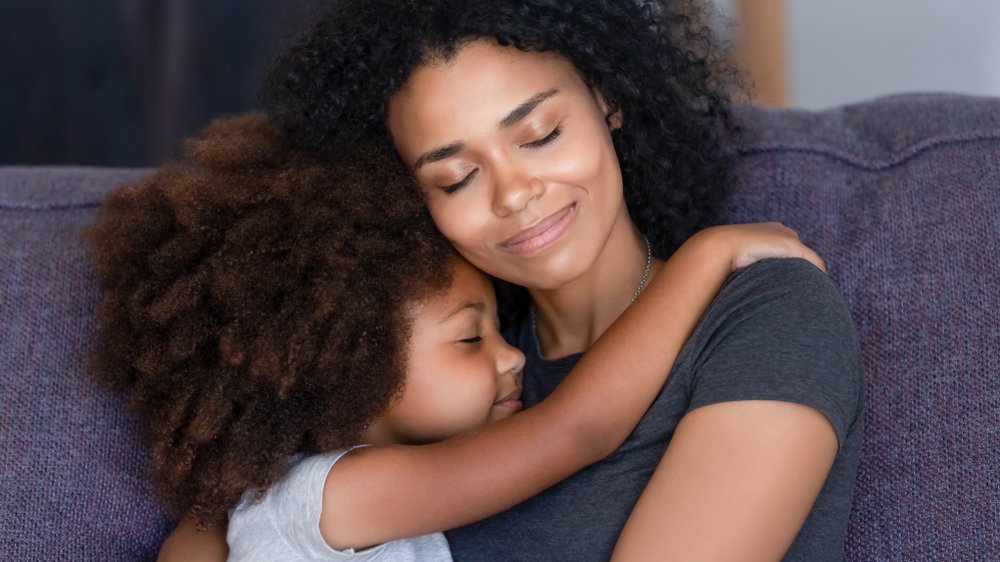 Uma mulher negra sendo abraçada por uma criança negra.
