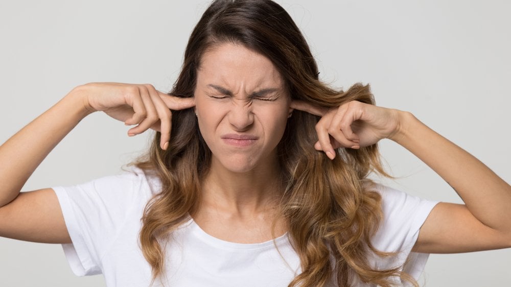 Uma mulher branca tapando seus ouvidos e franzindo a sua testa.